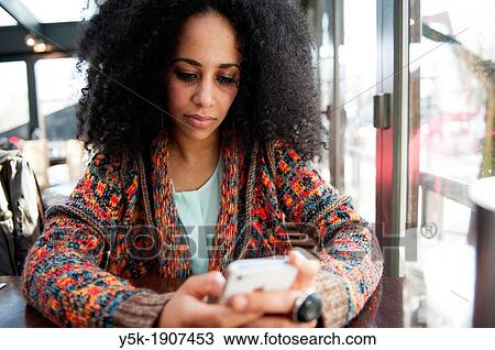 Rotterdam, Netherlands. Young, African woman reading messages on het iPhone, while sitting down at a restaurant table during lunchtime. View Large Photo Image Stock Image - Rotterdam, Netherlands. Young, African woman reading messages on het iPhone, while sitting down at a restaurant table during lunchtime.. Fotosearch