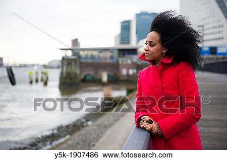 Rotterdam, Netherlands. Young, African woman with a red winter coat, pondering and looking out over the river, next to the Willemsbrug in Rotterdam. View Large Photo Image Stock Photograph - Rotterdam, Netherlands. Young, African woman with a red winter coat, pondering and looking out over the river, next to the Willemsbrug in Rotterdam.. Fotosearch
