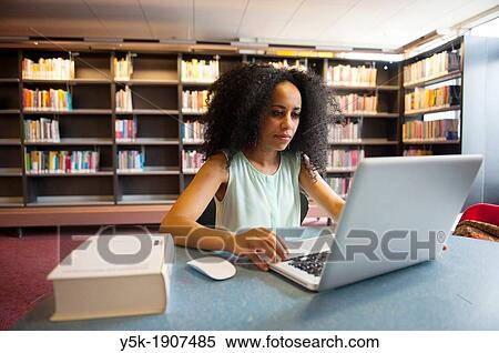 Rotterdam, Netherlands. Young African woman working with her notebook or laptop computer on a desk in a public library, with some educational literature at her disposal. View Large Photo Image Stock Photography - Rotterdam, Netherlands. Young African woman working with her notebook or laptop computer on a desk in a public library, with some educational literature at her disposal.. Fotosearch
