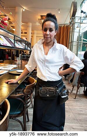 Stock Photograph - Rotterdam, Netherlands. Young, colored waitress serving a customer in a grand-cafe restaurant, down town Rotterdam.. Fotosearch