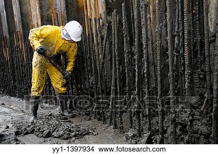 Rotterdam, Netherlands. Young man removing river mud from an underground construction site, after drainage of the pit. View Large Photo Image Picture - Rotterdam, Netherlands. Young man removing river mud from an underground construction site, after drainage of the pit.. Fotosearch