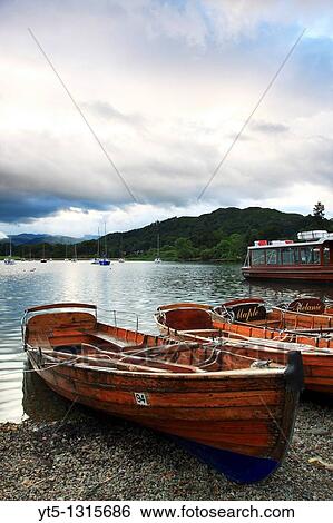 Rowing Boats moored on the shore of Windermere with Loughrigg Fell in the background, Waterhead, Lake District National Park, Cumbria, England View Large Photo Image Stock Photograph - Rowing Boats moored on the shore of Windermere with Loughrigg Fell in the background, Waterhead, Lake District National Park, Cumbria, England. Fotosearch
