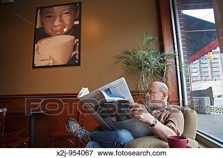 Stock Photo - Royal Oak, Michigan - A man reads a newspaper at Sweetwaters Cafe, a coffee shop. Fotosearch
