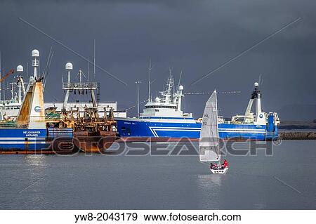 Stock Photo - Sailboat with large fishing trawlers in Reykjavik Harbor, Reykjavik, Iceland.. Fotosearch