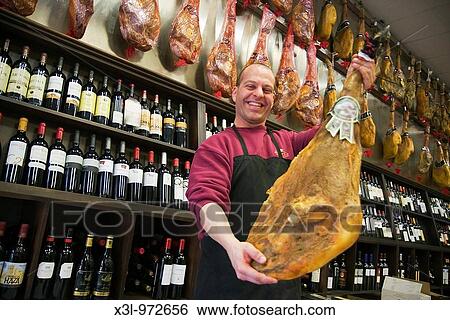Stock Photograph - Salesman in wine shop showing a cured ham. Fotosearch