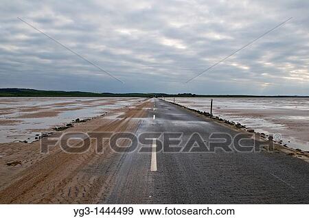 Stock Photo - Sand covered road to Lindisfarne - Holy island at low tide, Lindisfarne, England The road is only passable for a few hours around low tide, tidal charts are posted listing opening times. Fotosearch