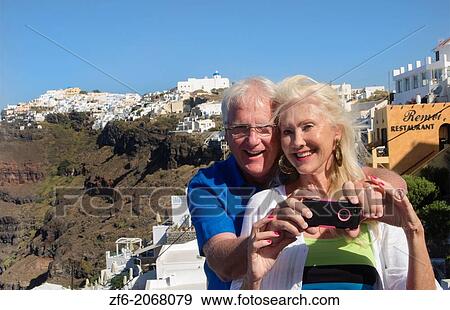 Santorini Greece retired couple on holiday having fun with cell phone pictures on cliff in Fira Greek vacation. View Large Photo Image Stock Photo - Santorini Greece retired couple on holiday having fun with cell phone pictures on cliff in Fira Greek vacation.. Fotosearch