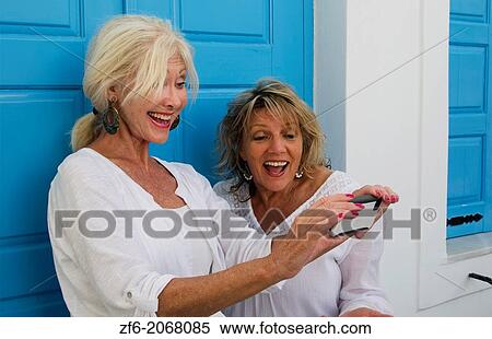 Stock Photography - Santorini Greece retired women on holiday having fun taking Iphone pictures at blue doors in Fira Greek vacation 12.. Fotosearch