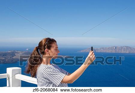 Santorini Greece young woman taking video with Iphone on holiday having fun on cliff in Fira Greek vacation 13. View Large Photo Image Picture - Santorini Greece young woman taking video with Iphone on holiday having fun on cliff in Fira Greek vacation 13.. Fotosearch