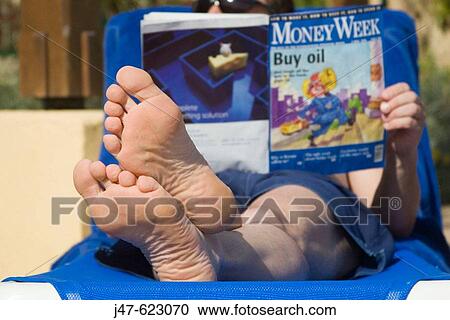 Selective focus on mans feet as he reads Money Week, magazine, on a sunlounger by a pool View Large Photo Image Stock Image - Selective focus on mans feet as he reads Money Week, magazine, on a sunlounger by a pool. Fotosearch