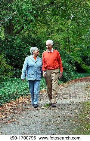 Stock Photograph - Senior caucasian couple looking at each other and walking hand in hand through the forest, blurred green background, Hamburg, Germany, Europe. Fotosearch