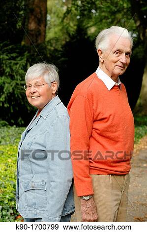 Stock Photo - Senior caucasian couple, looking happily at the camera, standing back to back to each other, blurred background, Hamburg, Germany, Europe. Fotosearch