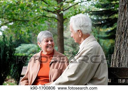 Senior caucasian couple sitting on a bench, trees in the background, looking at each other with one from front and one from behind, Hamburg, Germany, Europe View Large Photo Image Stock Photograph - Senior caucasian couple sitting on a bench, trees in the background, looking at each other with one from front and one from behind, Hamburg, Germany, Europe. Fotosearch