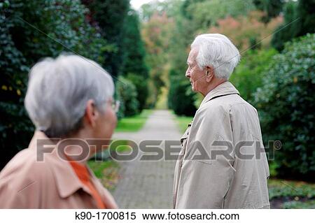 Stock Photography - Senior caucasian woman with glasses looking at senior man, seen from backside, blurred green background, Hamburg, Germany, Europe. Fotosearch