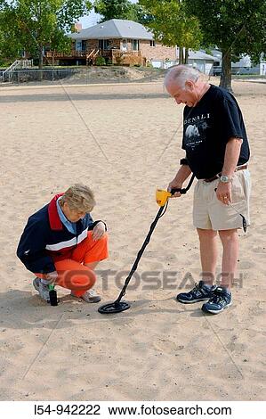 Stock Image - Senior Citizen couple scour a beach with a metal detector searching for burried treasures as a hobby. Fotosearch