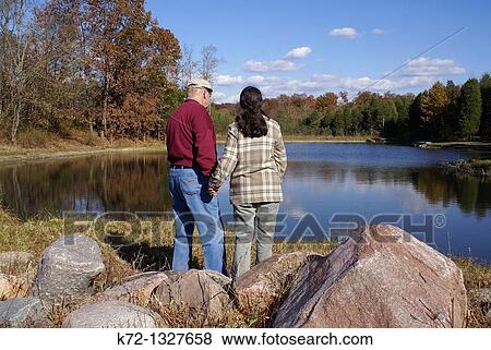 Senior couple holding hands looking at lake View Large Photo Image Stock Photo - Senior couple holding hands looking at lake. Fotosearch