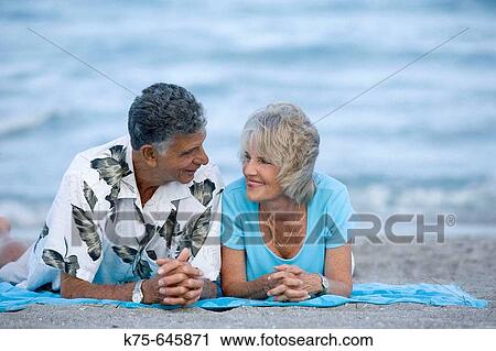 Stock Image - senior couple lying on beach towel. Fotosearch