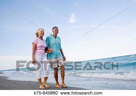 Stock Image - senior couple strolling along the beach. Fotosearch