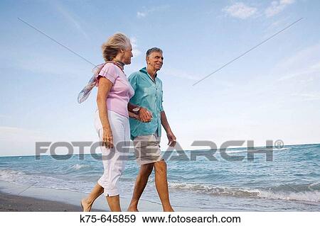 Stock Photo - senior couple walking along the beach. Fotosearch