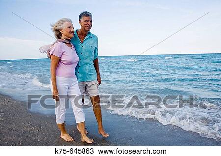 Stock Image - senior couple walking on beach. Fotosearch