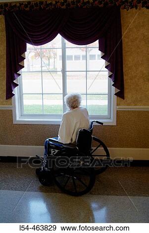 Stock Photo - Senior female woman sits and reads for relaxation and recreation and looks out a window while sitting in a wheelchair. Fotosearch