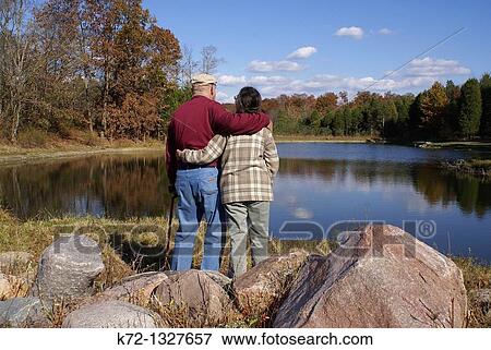 Senior man and woman standing looking at a lake in the fall View Large Photo Image Stock Photo - Senior man and woman standing looking at a lake in the fall. Fotosearch
