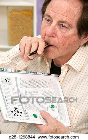 Picture - senior man doing crosswords to exercise his memory and fight Alzheimer disease. Fotosearch