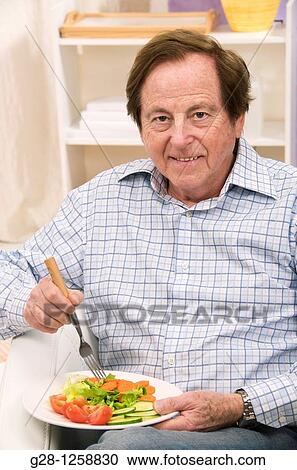 Stock Image - senior man eating a plate of tomato, carrot, and green salad. Fotosearch