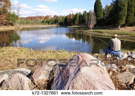 Stock Image - Senior man fishing alone on peaceful pond. Fotosearch