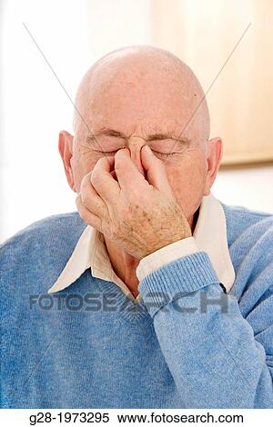 Stock Photography - Senior man in a blue pullover, holding his nose with his fingers for headache or sinusitis. Fotosearch