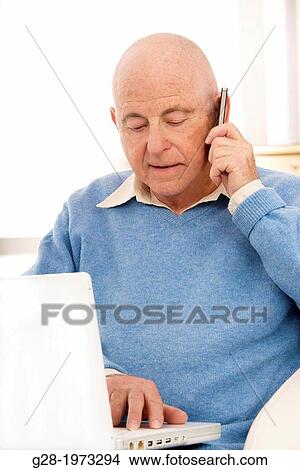 Senior man in a blue pullover using his phone and his laptop computer View Large Photo Image Picture - Senior man in a blue pullover using his phone and his laptop computer. Fotosearch