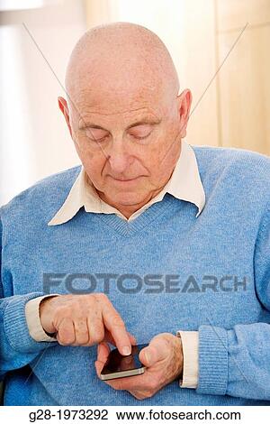 Stock Image - Senior man in a blue pullover, writing and sending a message on his phone. Fotosearch