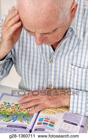 Stock Image - Senior man reading a book and exercising his memory withs tests to prevent Alzheimer disease. Fotosearch