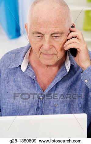Senior man using his computer and phoning with a cell phone at home View Large Photo Image Stock Photo - Senior man using his computer and phoning with a cell phone at home. Fotosearch