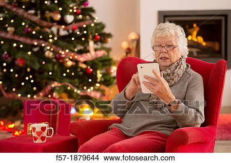 Senior woman communicating with family on her tablet computer at Christmas time View Large Photo Image Picture - Senior woman communicating with family on her tablet computer at Christmas time. Fotosearch