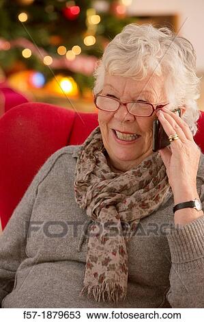 Stock Image - Senior woman communicating with family on her smart phone at Christmas time. Fotosearch