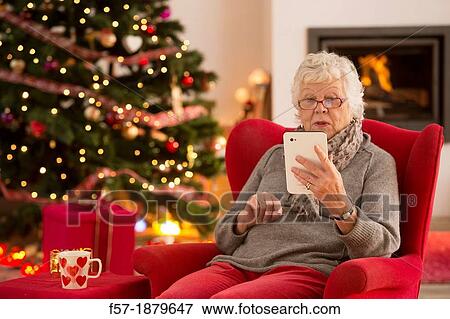 Senior woman communicating with family on her tablet computer at Christmas time View Large Photo Image Stock Photo - Senior woman communicating with family on her tablet computer at Christmas time. Fotosearch