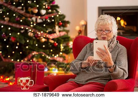 Senior woman communicating with family on her tablet computer at Christmas time View Large Photo Image Stock Photo - Senior woman communicating with family on her tablet computer at Christmas time. Fotosearch