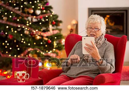 Senior woman communicating with family on her tablet computer at Christmas time View Large Photo Image Stock Photograph - Senior woman communicating with family on her tablet computer at Christmas time. Fotosearch