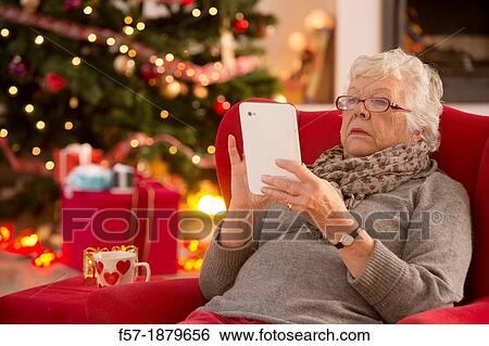 Senior woman communicating with family on her tablet computer at Christmas time View Large Photo Image Stock Photograph - Senior woman communicating with family on her tablet computer at Christmas time. Fotosearch
