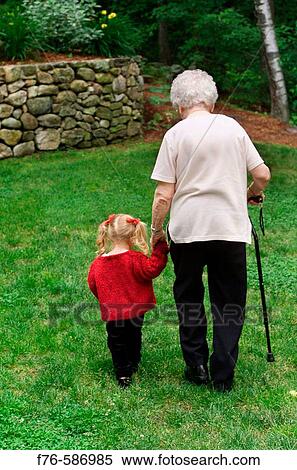 Stock Photography - Senior woman, grandmother, walking with cane across backyard lawn with her 3 year old granddaughter.. Fotosearch