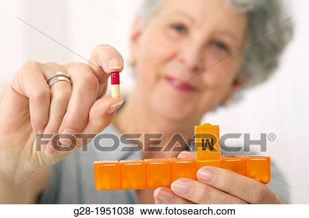 Senior woman holding a capsule in one hand and a pill distributor in the other View Large Photo Image Stock Photo - Senior woman holding a capsule in one hand and a pill distributor in the other. Fotosearch