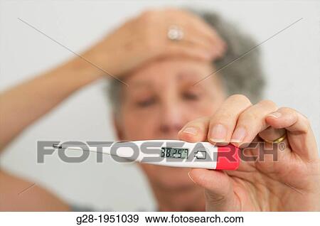 Senior woman holding a medical thermometer in one hand and her forehead in the other View Large Photo Image Stock Photo - Senior woman holding a medical thermometer in one hand and her forehead in the other. Fotosearch