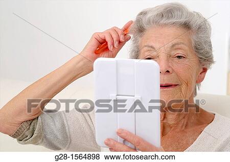 Senior woman holding a mirror and combing her hair View Large Photo Image Stock Photo - Senior woman holding a mirror and combing her hair. Fotosearch