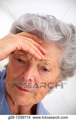 senior woman holding her forehead with a headache or not feeling well, or trying to remember something wearing a mauve cardigan at home View Large Photo Image Picture - senior woman holding her forehead with a headache or not feeling well, or trying to remember something wearing a mauve cardigan at home. Fotosearch