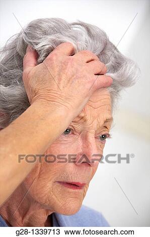senior woman holding her forehead with a headache or not feeling well, or trying to remember something wearing a mauve cardigan at home View Large Photo Image Stock Image - senior woman holding her forehead with a headache or not feeling well, or trying to remember something wearing a mauve cardigan at home. Fotosearch