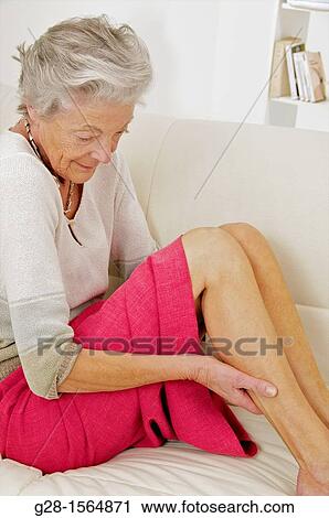 Senior woman holding her painful thigh on her sofa View Large Photo Image Stock Image - Senior woman holding her painful thigh on her sofa. Fotosearch