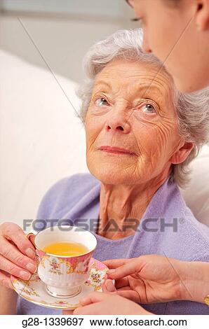 senior woman in a mauve cardigan, and young help giving her a cup of tea at home View Large Photo Image Stock Photo - senior woman in a mauve cardigan, and young help giving her a cup of tea at home. Fotosearch