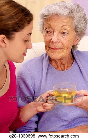 senior woman in a mauve cardigan, and young help giving her a cup of tea at home View Large Photo Image Stock Photo - senior woman in a mauve cardigan, and young help giving her a cup of tea at home. Fotosearch