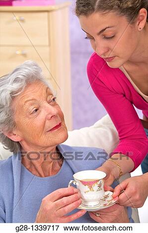 senior woman in a mauve cardigan, and young help giving her a cup of tea at home View Large Photo Image Stock Photo - senior woman in a mauve cardigan, and young help giving her a cup of tea at home. Fotosearch